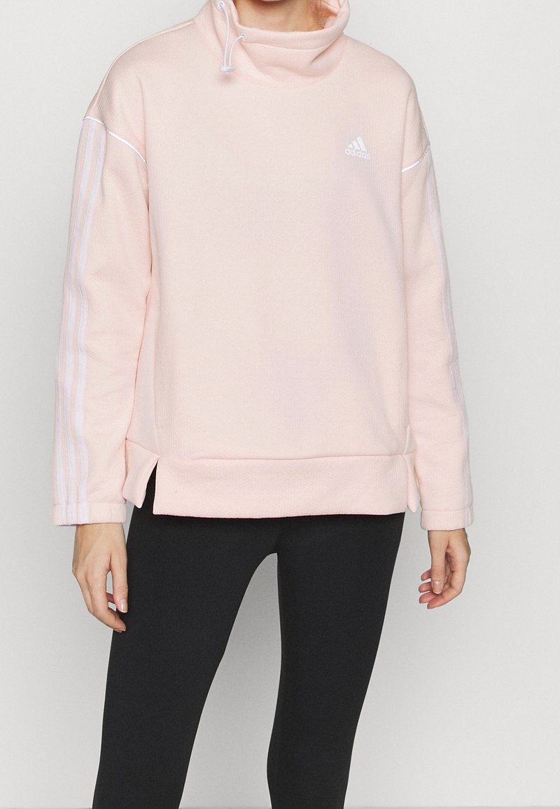 Sweat à capuche rose avec un col montant, en tissu doux et texturé, présentant des rayures blanches sur les manches et un logo Adidas.