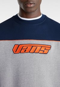 Grå och marinblå sweatshirt med en broderad orange "VANS"-logotyp. Har en rundad halsringning och textil med struktur i en tvåtoners design.