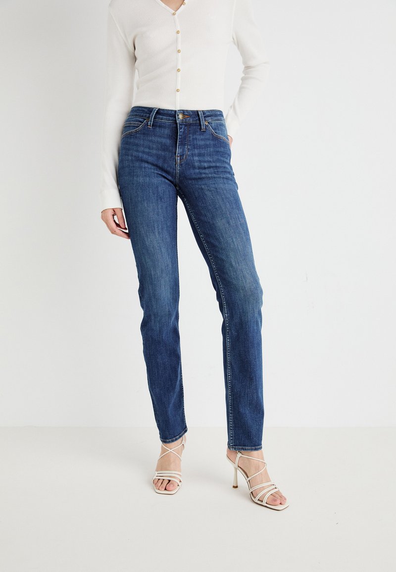 Jeans in denim blu a vita alta con gamba dritta, dotati di dettagli in metallo dorato, cuciture sottili e una texture liscia. Un paio di tacchi a strappo.
