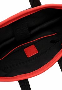 Schwarzes Tascheninnere mit roten Akzenten, einer schwarzen Reißverschlusstasche und einem roten Logo-Patch. Strukturierte Träger und glatte Innenauskleidung.