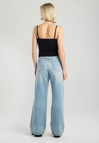 Black knit tank top with scalloped edges, paired with light blue wide-leg denim jeans featuring a faded design and two back pockets.