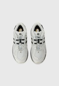 Ș shoes-uri atletice gri deschis cu un partea superioară din plasă, accente negre, șireturi plate și o talpă texturată, având detalii cu logo pe limbă și pe lateral.