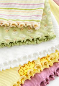 Set aus fünf gerippten Stoffstücken in Pastellfarben: gestreift in Gelb/Pink, grün mit Blumenmuster, weiß, gelb mit Blütendetail und pink. Jedes hat gewellte Kanten.