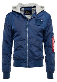 Mörkblå bomberjacka med grå huva, dragkedja framtill, ribbade ärmslut och nederkant, flera fickor och en röd etikett "Remove Before Flight".