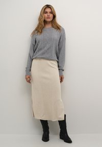 Pull en tricot côtelé gris clair avec des manches longues, associé à une jupe maxi crème à côtes et des bottes noires jusqu'aux genoux.