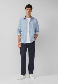 Jasnoniebieska koszula na guziki z drobnym nadrukiem, zestawiona z białym t-shirtem z okrągłym dekoltem, ciemnogranatowymi spodniami i białymi trampkami.