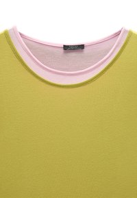 T-shirt z okrągłym dekoltem w jednolitym limonkowym kolorze z różowym wykończeniem dekoltu. Gładki materiał o lekko połyskującej fakturze.