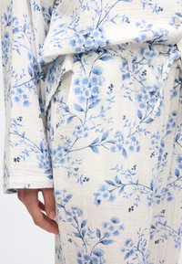 Ensemble de vêtements d'intérieur à motifs floraux bleus, fabriqué en tissu doux et texturé. Comprend une taille à cordon de serrage et un bouton décoratif sur le haut.