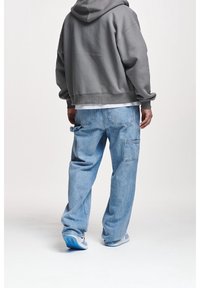 Sudadera gris con un corte relajado y bolsillo canguro, combinada con jeans baggy de color azul claro que tienen bolsillos laterales y una textura desgastada.
