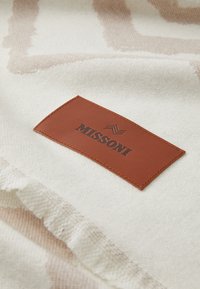 Țesătură crem texturată cu modele abstracte de culoare maro deschis, având o etichetă dreptunghiulară din piele maro, imprimată cu "MISSONI."