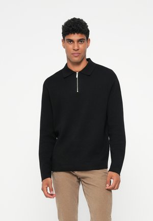 Sort pullovertrøje med lynlåskrave, lange ærmer og tekstureret strik. Sammenstylet med beige fløjlsgamasjer.
