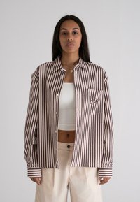 Stribet button-up skjorte i hvid og burgunder, med en lomme og et logo-detalje. Materialet ser ud til at være vævet med en blød tekstur.