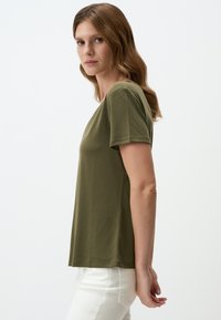 T-shirt a maniche corte verde oliva in tessuto morbido con vestibilità rilassata, scollatura rotonda e orlo cucito, abbinato a pantaloni bianchi.