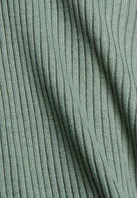 Gros plan sur un tissu côtelé vert sauge doux avec une texture tricotée verticale et de légers plis créant des ombres et de la profondeur.
