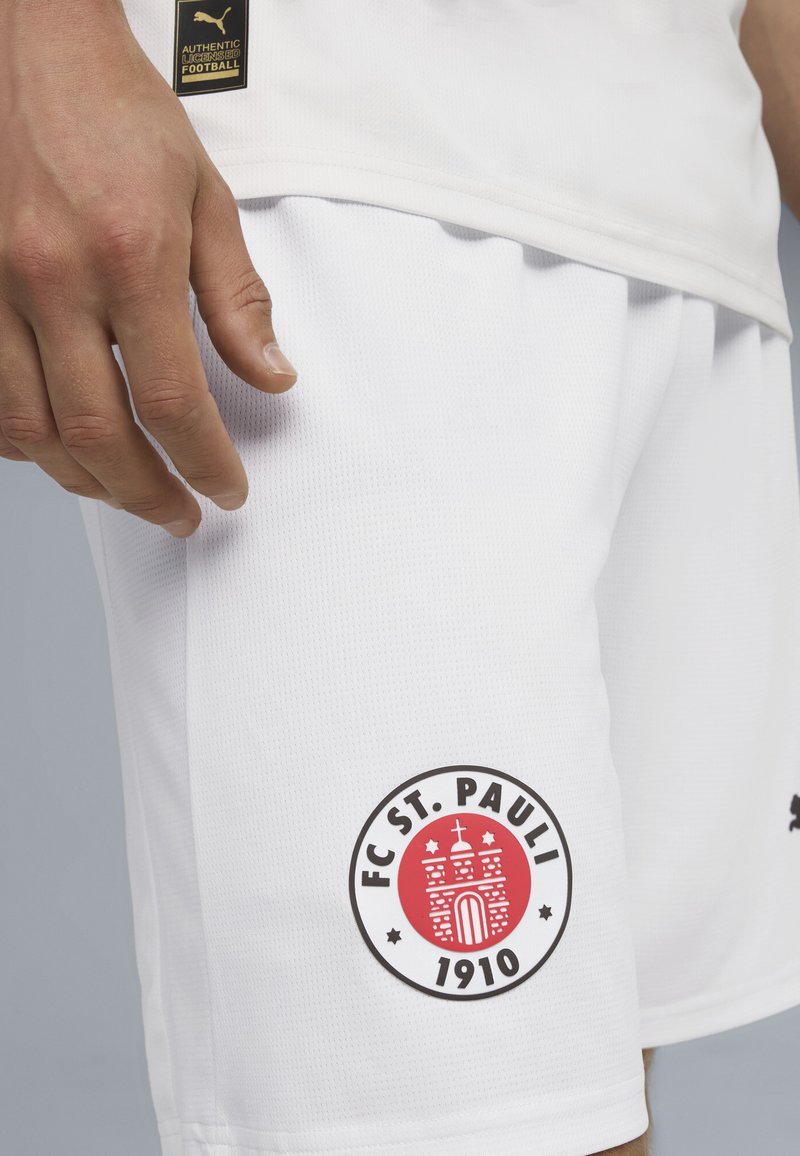 Biele futbalové šortky vyrobené z priedušného materiálu, s okrúhlym červeným a čiernym logom FC St. Pauli na ľavom stehne.