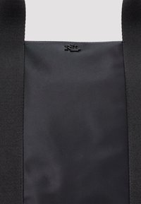 Fekete tote táska sima anyagú felülettel, két masszív fogantyúval és dombornyomott logó részlettel. Egyszerű és minimalista dizájn.