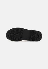 Semelle d'une chaussure présentant une surface en caoutchouc noir texturé avec un design de grip à motifs et plusieurs rainures de profil pour adhérence.