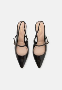 Juodos lakinės odos slingback moteriškos bateliai su smailiais kojų pirštais, kūno spalvos pado vidumi ir dviguba dirželių sistema su auksinės spalvos sagtimi.