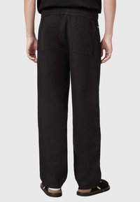 Pantalons en coton noirs avec une coupe décontractée, une taille élastique et deux poches arrière. Le tissu semble doux avec une finition mate.