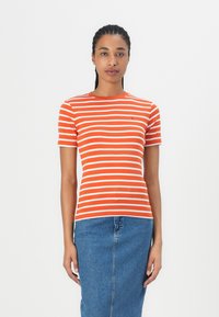Oransje og hvitstripet t-skjorte med rund hals og korte ermer, sammen med et denimblått skjørt. Laget av bomull.