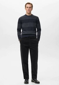 Maglione a righe blu scuro in maglia con scollatura rotonda, abbinato a pantaloni in velluto a coste neri e scarpe nere. Design semplice, silhouette aderente.
