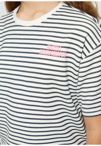 Pasiasty bawełniany t-shirt z granatowymi i białymi poziomymi liniami, z różowym haftowanym napisem „Distant Dreams” na lewej stronie klatki piersiowej.