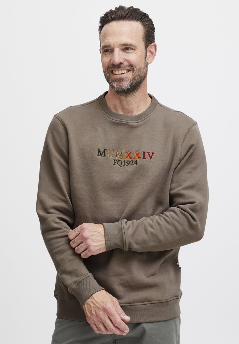Brun bomullssweatshirt med rund hals og ribbede mansjetter. Brodert tekst "MCMXXIV FQ1924" i forskjellige farger på forsiden.