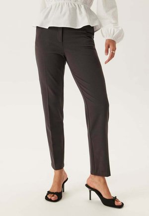 Pantaloni tailored grigi scuri con una vestibilità elegante, texture liscia e dettagli di piega sottili, abbinati a mule nere con tacco alto.