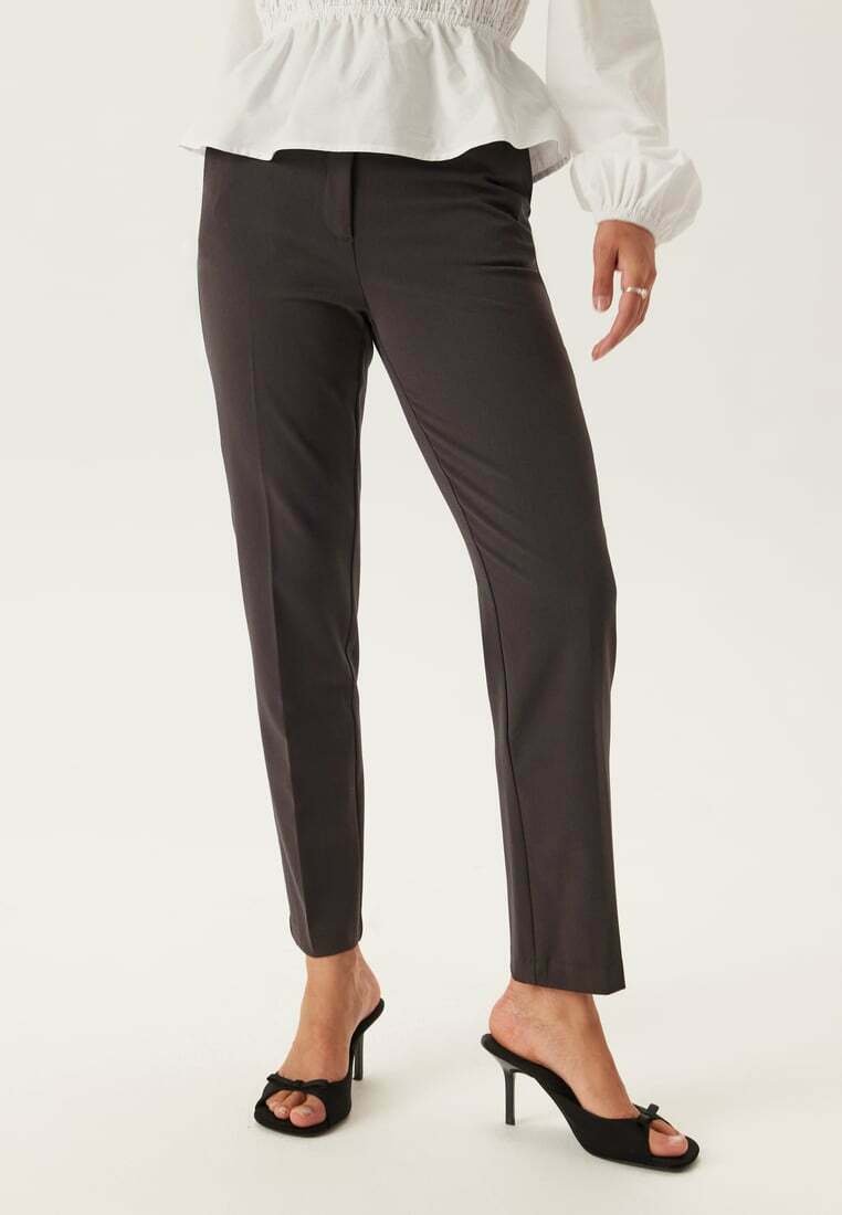 Donkergrijze op maat gemaakte broek met een slanke pasvorm, gladde textuur en subtiele plooi-details, gecombineerd met zwarte hoge muiltjes.