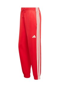 Crvene atletske hlače s bijelim bočnim crtama, elastičnim pojasom s vezicom, sužene na gležnjevima i s logom Adidasa u bijeloj boji na lijevoj nozi.