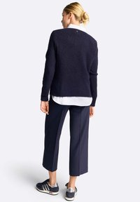 Maglione navigazione con finitura testurizzata, scollatura rotonda e maniche lunghe, indossato sopra una camicia bianca; abbinato a pantaloni cropped blu e sneaker.