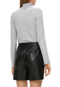 Pull en col roulé gris à manches longues, associé à un short en cuir noir taille haute avec poches arrière et texture lisse.