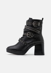 Botines negros de cuero, con múltiples hebillas y tachuelas, un tacón grueso y un diseño de punta afilada.