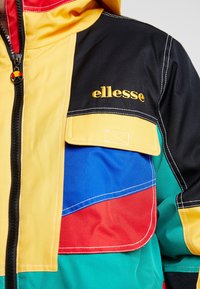 Färgglad jacka med gula, svarta, blå, röda och gröna paneler. Inkluderar dragkedjestängning, huva och broderad "ellesse"-logotyp.
