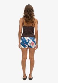 Top de punto marrón sin mangas con tirantes finos, combinado con pantalones cortos blancos con un vibrante patrón de hojas tropicales en azul y rosa.