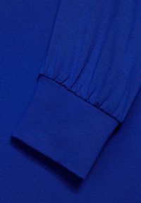 Blå långärmad plagg med en rynkad manschett. Tyget är slätt och ger en lätt lyster. Manschetten är elastisk för en snug passform.