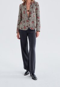 Kavaj i krämfärg med svart och röd paisleymönster, dubbelknäppt design, matchad medvida svarta byxor och glansiga svarta stövlar.