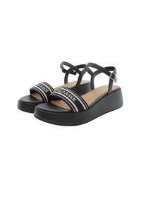 Czarne sandały na koturnie z krzyżującymi się paskami, z markowym paskiem z białymi akcentami, gładką fakturą i płaską gumową podeszwą.