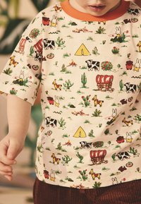 Kortærmet bomulds-t-shirt med farverige tegneseriemønstre af dyr og kaktusser på en cremefarvet baggrund, med en orange ribstrikket krave.