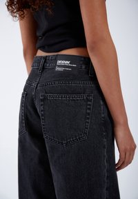 Black denim jeans with a high waist, featuring a rectangular patch label on the back. The fabric shows a smooth, slightly distressed texture.