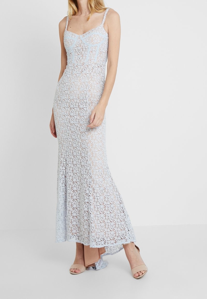 Robe en dentelle bleu clair avec motif floral, corsage ajusté, bretelles fines et ourlet évasé. Associée à des escarpins couleur nude.