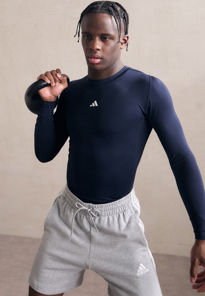 Jūrų karinės ilgomis rankovėmis sportinė maikutė, pilkos spalvos trumpai. Modelis laiko juodą girą. Adidas logotipas matomas ant maikutės ir šortų. Lygus paviršius.