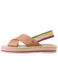 Sandale en cuir tan avec un design à lanières croisées, semelle en jute tressé et une sangle de talon élastique rayée multicolore. Accent rouge et blanc sur la semelle.