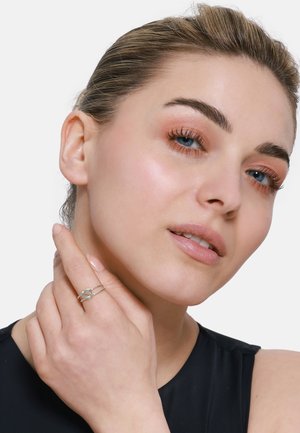 Silver ring with intertwined design. Model wearing it on the right hand, displaying a smooth, polished surface. Light skin tone, neutral makeup.
