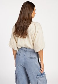 Lichtbeige textuur top met pofmouwen, gecombineerd met hoge blauwe denim cargo pantalons met zakken en stiksels.