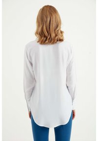 Witte blouse met lange mouwen, een gebogen zoom en een gladde textuur, met knoopmanchetten en een relaxed fit ontwerp.