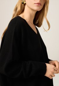 Schwarzer V-Ausschnitt-Pullover mit langen, lockeren Ärmeln aus weichem Strickmaterial. Auffällige gerippte Bündchen und lockere Passform.