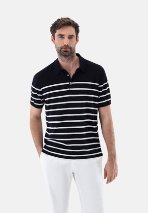 Polo navy con righe orizzontali bianche, maniche corte e colletto con tre bottoni. Abbinato a pantaloni bianchi per un contrasto.