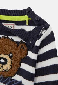 Navy and white striped sweater featuring a textured brown bear motif, button details on the shoulder, and a bright green inner lining.