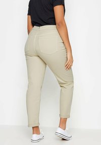 Beige tapered farkut, joissa on käännetyt lahkeet, takataskut ja keskipitkä vyötärö, yhdistettynä valkoisiin lenkkareihin. Suora puuvillakangas.